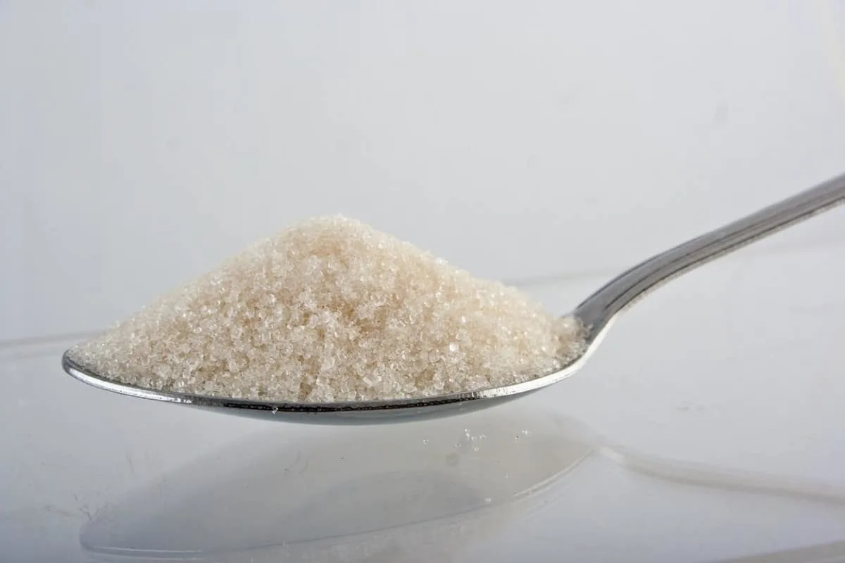 A photo of added sugar in a spoon, with a white background.