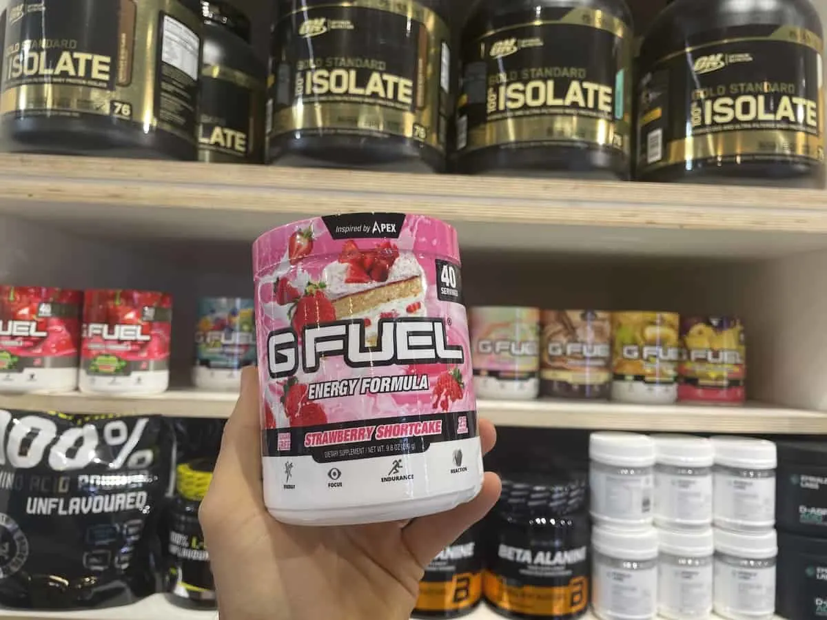 G Fuel Strawberry Shortcake energy tub held in hand with different flavors of G Fuel in background