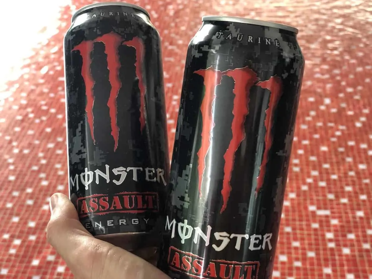 A photo of Monster energy assault flavor in a red and white background, the drink is held in a hand