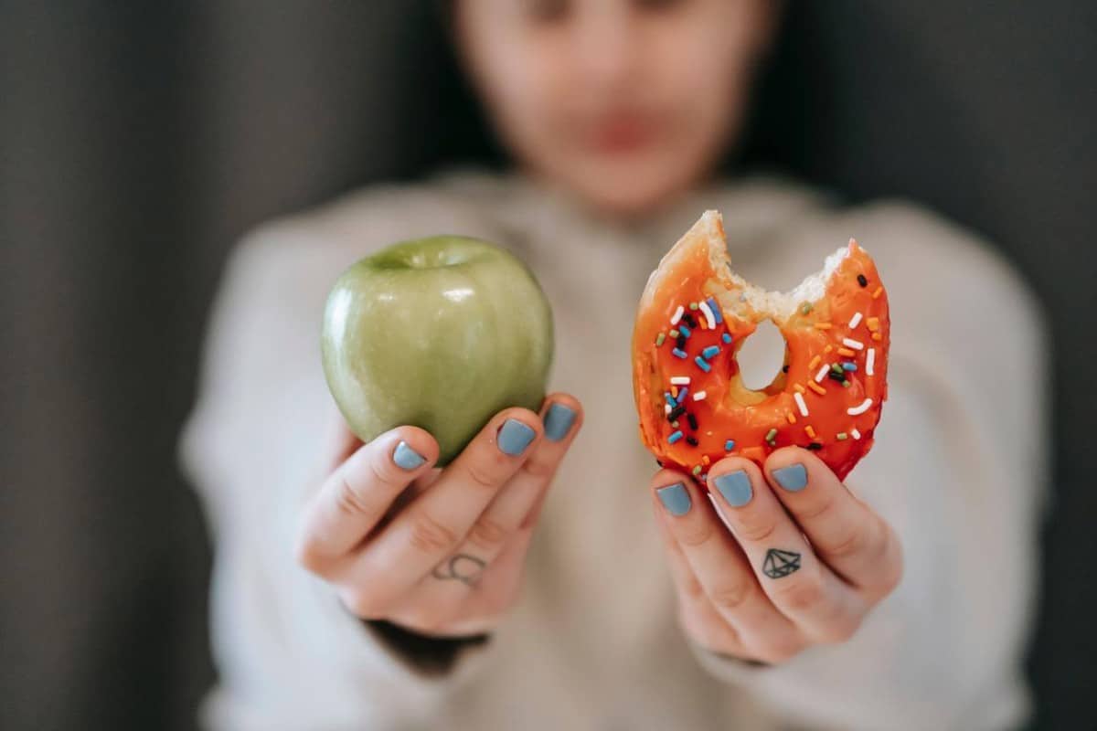 A woman showing a piece of apple and a piece of doughnut.