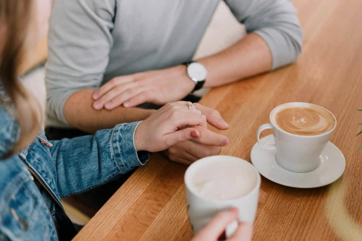 A couple holding each other ,hands having a coffee.