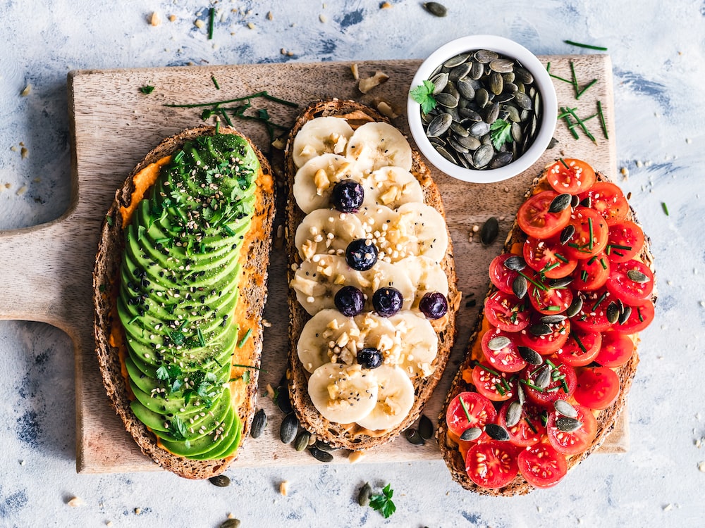 Different kinds of fruits and vegetables on a piece of bread on a cutting board